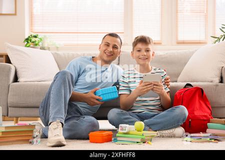 Père avec boîte à lunch scolaire et son petit fils emballant sac à dos à la maison Banque D'Images