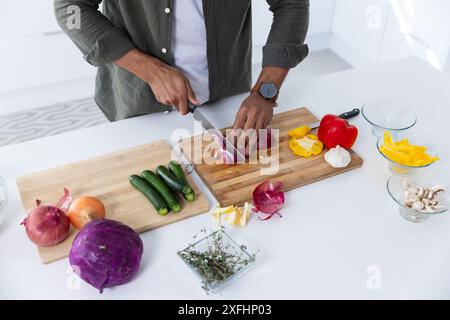 Hacher des légumes sur une planche à découper, homme préparant des ingrédients dans la cuisine Banque D'Images