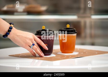 Main de femme tenant du jus. cocktail et boisson non alcoolisée dans une tasse en papier Banque D'Images