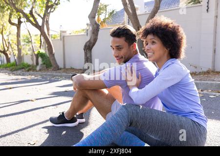 Assis sur le trottoir, couple se reposant après l'entraînement en plein air, souriant et détendu Banque D'Images