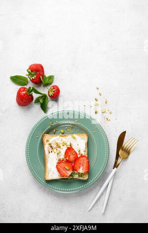 Sandwich avec fraises, fromage à pâte molle, pistaches sur plaque verte sur fond blanc. Vue de dessus. copier l'espace Banque D'Images