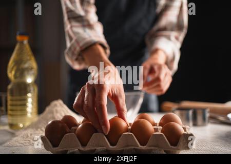 Mains féminines ramassant l'oeuf du carton tout en préparant des ingrédients pour la cuisson maison. Concept de cuisson maison Banque D'Images