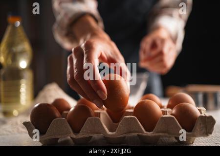 Mains féminines ramassant l'oeuf du carton tout en préparant des ingrédients pour la cuisson maison. Concept de cuisson maison Banque D'Images