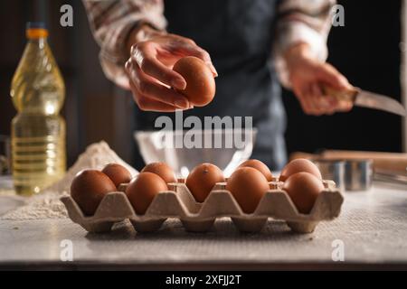 Main de la femme ramassant l'oeuf du carton pour la cuisson à la maison, gros plan avec l'accent sur l'oeuf et le carton. Ingrédients de cuisson disposés sur la table Banque D'Images