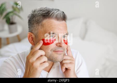 un homme applique des patchs hydratants avec des vitamines sous ses yeux, un produit cosmétique moderne pour les yeux pour lisser les fines rides et éliminer les rougeurs Banque D'Images