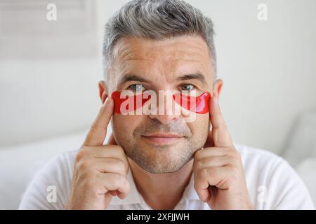 un homme applique des patchs hydratants avec des vitamines sous ses yeux, un produit cosmétique moderne pour les yeux pour lisser les fines rides et éliminer les rougeurs Banque D'Images