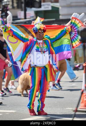 Une personne vêtue d'une tenue arc-en-ciel vibrante célébrant lors d'un défilé de fierté dans une rue de la ville Banque D'Images