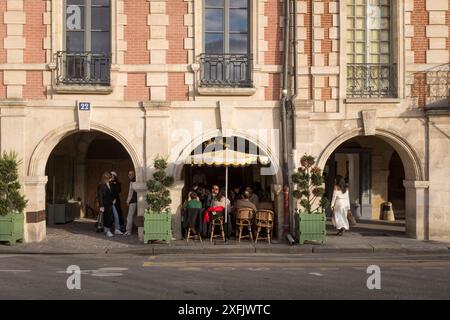 Les convives profitent du soleil couchant sous les arches du Café Hugo au large de la place des Vosges, à Paris, France. Banque D'Images