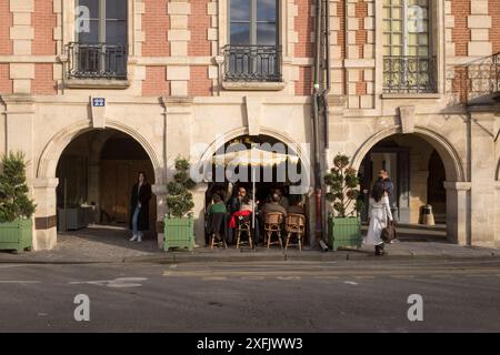 Les convives profitent du soleil couchant sous les arches du Café Hugo au large de la place des Vosges, à Paris, France. Banque D'Images