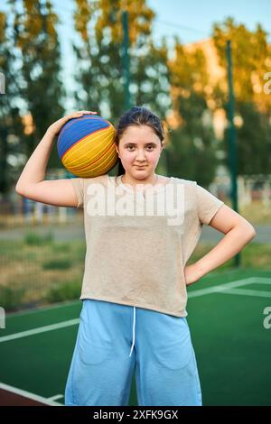 Portrait de style de vie de petite fille caucasienne joyeuse de dix ans tenant le ballon de jeu pour le basket-ball en plein air à la chaude journée d'été. Mode de vie actif, entraînez-vous Banque D'Images