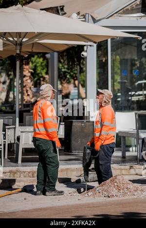 Deux ouvriers de la route dans des gilets réflecteurs utilisant le marteau, le forage, la rupture de l'asphalte. Discussion. Réparation de routes Banque D'Images