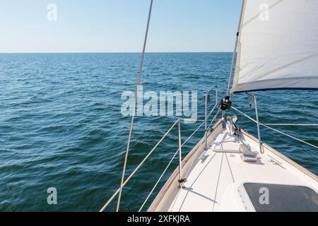 Yacht blanc naviguant sur une journée d'été ensoleillée. Vue de dessus du pont à la proue, au mât et aux voiles. Vagues et éclaboussures d'eau. Ciel bleu clair. Golfe de F. Banque D'Images