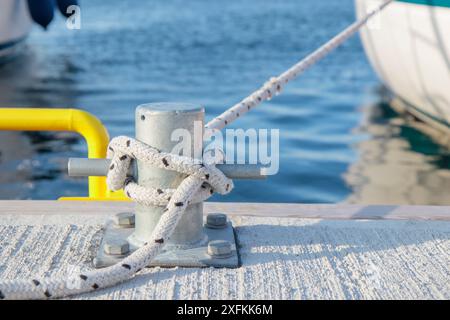 Corde blanche avec attaché autour d'un taquet sur une jetée. Corde d'amarrage nautique avec un bateau sur le fond Banque D'Images