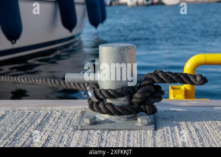 Corde noire avec noué autour d'un taquet sur une jetée. Corde d'amarrage nautique avec un bateau sur le fond Banque D'Images