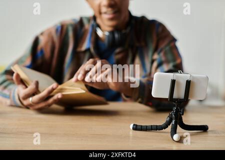 Homme afro-américain lit le livre tout en vlogging sur le trépied du téléphone. Banque D'Images