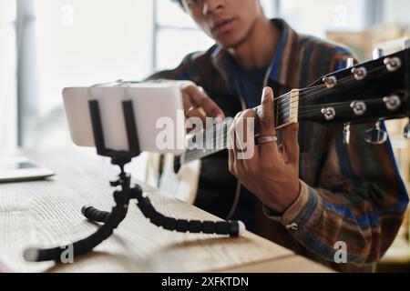 Homme joue de la guitare devant le téléphone tout en enregistrant un vlog. Banque D'Images