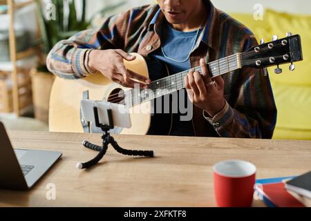 Jeune blogueur afro-américain joue de la guitare tout en parlant sur la caméra du téléphone. Banque D'Images