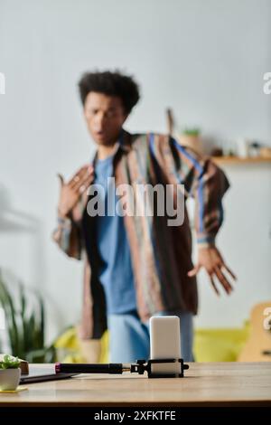 Un jeune blogueur afro-américain se tient devant une table, parlant avec la caméra de son téléphone. Banque D'Images
