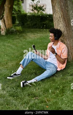 Un jeune homme afro-américain assis sous un arbre, engrossé dans son téléphone. Banque D'Images