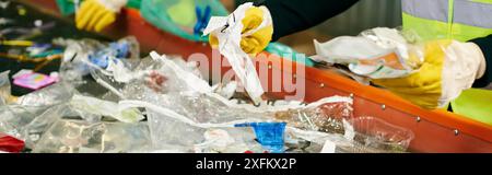 Une personne dans un gilet de sécurité jaune ramassant des bouteilles en plastique, avec de jeunes bénévoles, triant les ordures pour les recycler. Banque D'Images