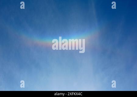 Le jet liner passe sous un « arc nuageux » causé par des cristaux de glace dans les nuages élevés réfractant la lumière du soleil couchant. Surrey, Angleterre, Royaume-Uni, avril. Banque D'Images