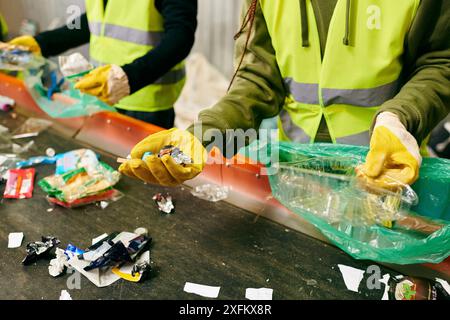 Groupe de jeunes volontaires éco-conscients en gilets de sécurité jaunes nettoyant une table ensemble, triant les ordures. Banque D'Images