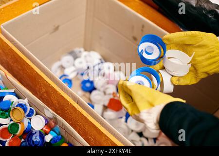 Un jeune volontaire portant un gant jaune tient soigneusement une paire de gants assortis au-dessus d'une boîte de déchets, montrant sa conscience écologique. Banque D'Images