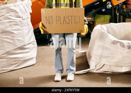 Le jeune bénévole en gants et gilet de sécurité tient un panneau indiquant qu'il n'y a pas de plastique lors du tri des déchets. Banque D'Images