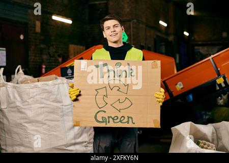 Un jeune bénévole en gants et gilet de sécurité tient une pancarte qui dit penser vert tout en triant les déchets. Banque D'Images