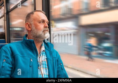 portrait d'un homme barbu dans une veste bleue parlant au téléphone dans un bus ou un tram. Concept de style de vie Banque D'Images