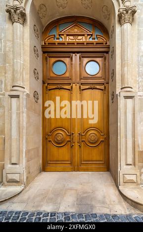 Une paire de portes en bois finement sculptées, avec des fenêtres circulaires et des moulures décoratives, serties dans une arche en pierre Banque D'Images