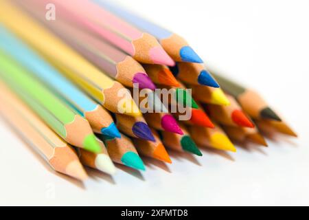 Une image en gros plan d'un groupe de crayons de couleur en bois disposés dans un motif triangulaire avec les extrémités aiguisées pointant vers le haut sur un fond blanc. Le Banque D'Images