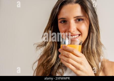 Femme souriante tenant un verre de jus d'orange frais, profitant d'une boisson saine - expression lumineuse et heureuse - beauté naturelle et boisson rafraîchissante. Banque D'Images