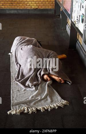 Obdachloser, spärlich bekleidet und Barfuß, schläft auf seinem kargen Lager, bestehend aus zwei Decken auf dem kalten Fliesenboden - Berlin, Deutschland, GER, Allemagne, 26.06.2024 - Berlin-Mitte Ortsteil Wedding : Die Lagerstätte des Obdachlosen befindet sich am Eingang einer S-Bahnstation. Die angrenzenden Straßen sind zu einem Anlaufpunkt für die Alkohol- und Drogenszene geworden, insbesondere trifft sich hier seit geraumer Zeit die crack-Szene. Immer mehr Menschen leben in Berlin ohne festen Wohnsitz auf der Straße. *** Homme sans-abri, à peine vêtu et pieds nus, dort sur son maigre camp, contre Banque D'Images