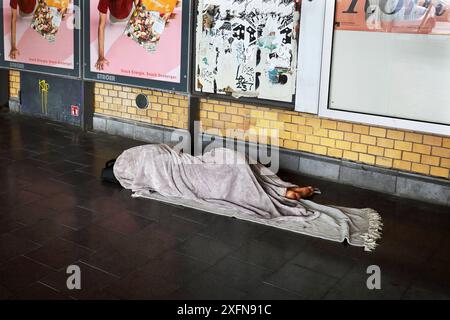 Obdachloser, spärlich bekleidet und Barfuß, schläft auf seinem kargen Lager, bestehend aus zwei Decken auf dem kalten Fliesenboden - Berlin, Deutschland, GER, Allemagne, 26.06.2024 - Berlin-Mitte Ortsteil Wedding : Die Lagerstätte des Obdachlosen befindet sich am Eingang einer S-Bahnstation. Die angrenzenden Straßen sind zu einem Anlaufpunkt für die Alkohol- und Drogenszene geworden, insbesondere trifft sich hier seit geraumer Zeit die crack-Szene. Immer mehr Menschen leben in Berlin ohne festen Wohnsitz auf der Straße. *** Homme sans-abri, à peine vêtu et pieds nus, dort sur son maigre camp, contre Banque D'Images