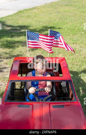 Austin, Texas, États-Unis. 4 juillet 2024. Un garçon assis dans une voiture jouet avec des drapeaux américains qui volent est assis à Barton Hills Elementary pendant le défilé annuel du quartier de Barton Hills le 4 juillet dans le sud d'Austin, Texas, le 4 juillet 2024. Quelques centaines de résidents ont parcouru le défilé de 1/2 km jusqu'à l'école primaire et ont dégusté des biscuits, de la pastèque et de la crème glacée. (Crédit image : © Bob Daemmrich/ZUMA Press Wire) USAGE ÉDITORIAL SEULEMENT! Non destiné à UN USAGE commercial ! Banque D'Images