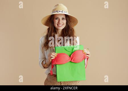 Vacances à la plage. femme moderne souriante en blouse blanche et short sur fond beige avec bikini et chapeau d'été. Banque D'Images