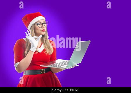 Jeune Père Noël faisant un geste OK en regardant un contenu sur un ordinateur portable isolé sur fond violet Banque D'Images