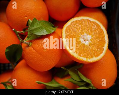 Un panier d'oranges avec une coupe ouverte. Les oranges sont mûres et prêtes à manger. Le panier est plein d'oranges, avec certains d'entre eux encore attachés au t Banque D'Images