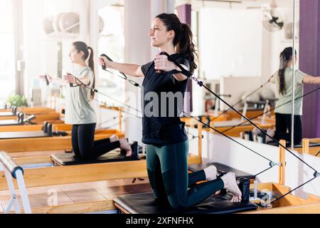 Deux jeunes femmes en forme qui forment des pilates sur un lit réformateur. Machine studio Reformer Pilates pour les exercices de fitness dans la salle de gym. Concept fitness. Sain an Banque D'Images