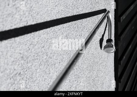 Cette photographie en noir et blanc capture l'interaction de l'ombre et de la lumière sur un mur texturé. Le contraste saisissant souligne les motifs et les textures Banque D'Images