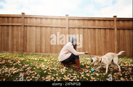 Femme, chien et jouer avec la balle dans la cour arrière pour lier, enseigner des trucs et apprendre à la maison. Dame, labrador et animal de compagnie dans la nature avec obéissance Banque D'Images