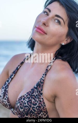 Cette image capture un moment radieux sur une plage ensoleillée. Une femme brune dans un maillot de bain se tient sur le shor sablonneux Banque D'Images