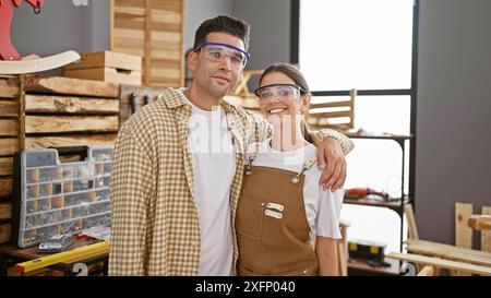 Homme et femme menuisiers dans l'atelier serrant et souriant avec des outils et du bois en arrière-plan Banque D'Images