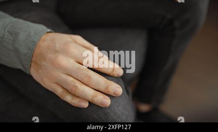Gros plan des mains d'un homme assis reposant sur son genou dans un cadre intérieur flou. Banque D'Images