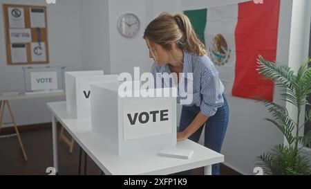 Une jeune femme jette son bulletin de vote dans une cabine de vote à l'intérieur d'une pièce ornée du drapeau mexicain. Banque D'Images