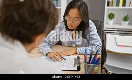 Une femme et un homme collaborent à l'intérieur dans un bureau, examinant des documents sur un bureau. Banque D'Images