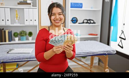 Une femme souriante tient des reais brésiliens dans la salle de traitement d'une clinique de physiothérapie. Banque D'Images