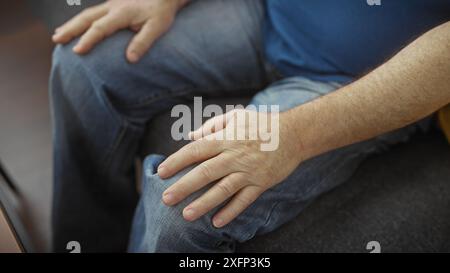 Gros plan des mains d'un homme d'âge moyen reposant sur ses genoux, représentant un moment franc à l'intérieur. Banque D'Images