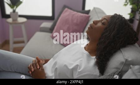 Une belle jeune femme afro-américaine avec les cheveux bouclés dormant paisiblement sur un canapé dans un cadre de salon confortable. Banque D'Images